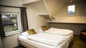 A bedroom with two beds, a window with curtains, and a view of a house outside.