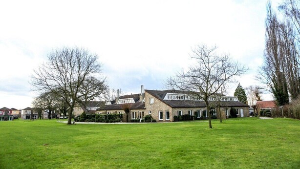A large, two-story building with a symmetrical facade, multiple chimneys, and a well-maintained lawn in the foreground.