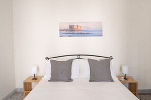 A neatly made bed with two pillows, a picture of a coastal building on the wall, and two bedside tables with lamps. - A Casa di Antonio by Wonderful Italy (Naples)