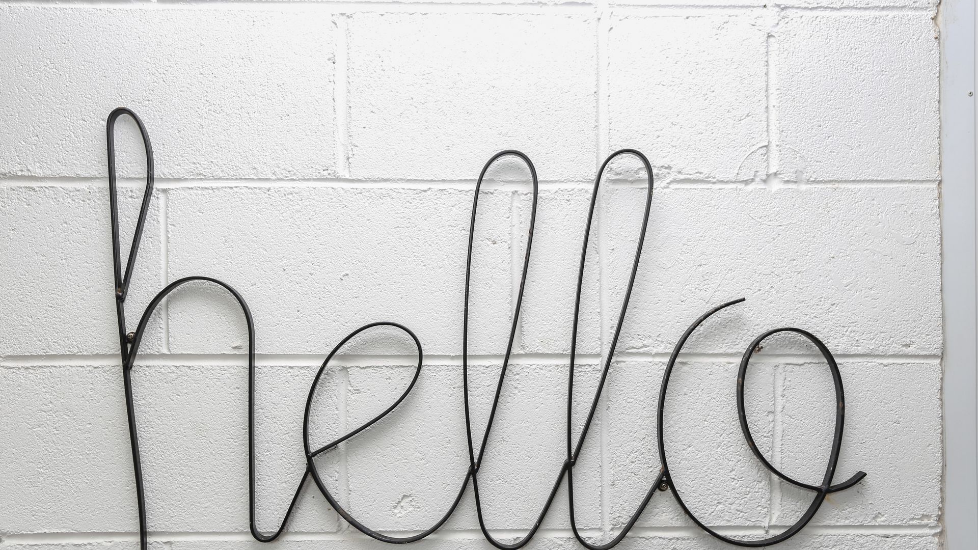 A wireframe 'hello' sign against a white brick wall.