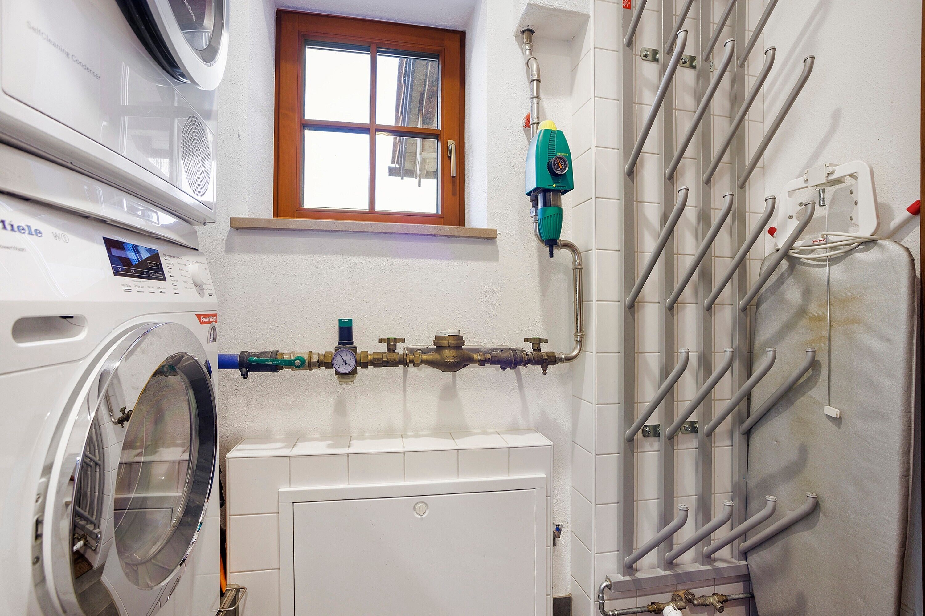 Une buanderie équipée d’un lave-linge, d’une fenêtre et d’un chauffe-eau doté de plusieurs tuyaux.