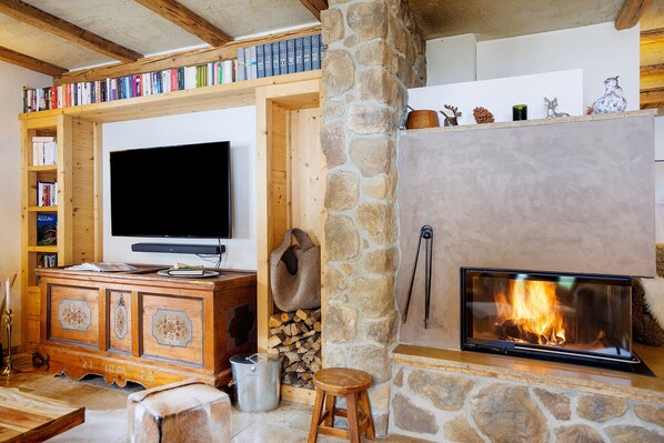 A cozy living room with a stone fireplace, a television, and a bookshelf filled with books.