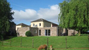 A two-story house with a stone facade, a large lawn, and a horse grazing. - Bungalowpark Landsrade - Vrijstaande bungalow 10 (Gulpen)