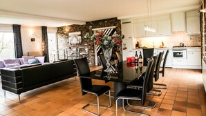 A modern kitchen with white cabinets, a black dining table, and a stone accent wall. - Bungalowpark Landsrade - Vrijstaande bungalow 10 (Gulpen)