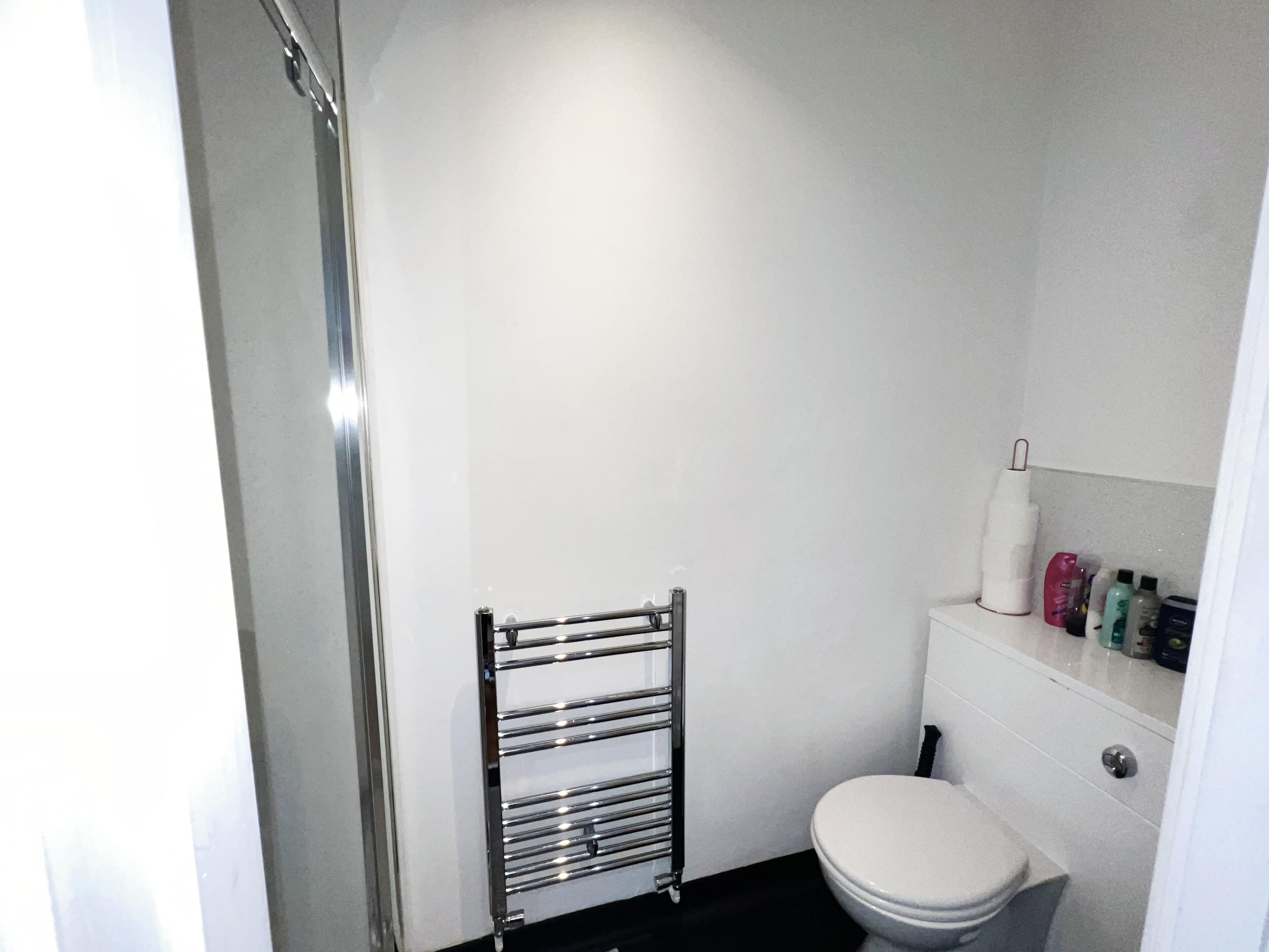 Une petite salle de bain moderne avec des toilettes blanches, un porte-serviettes chromé et une étagère contenant des articles de toilette.