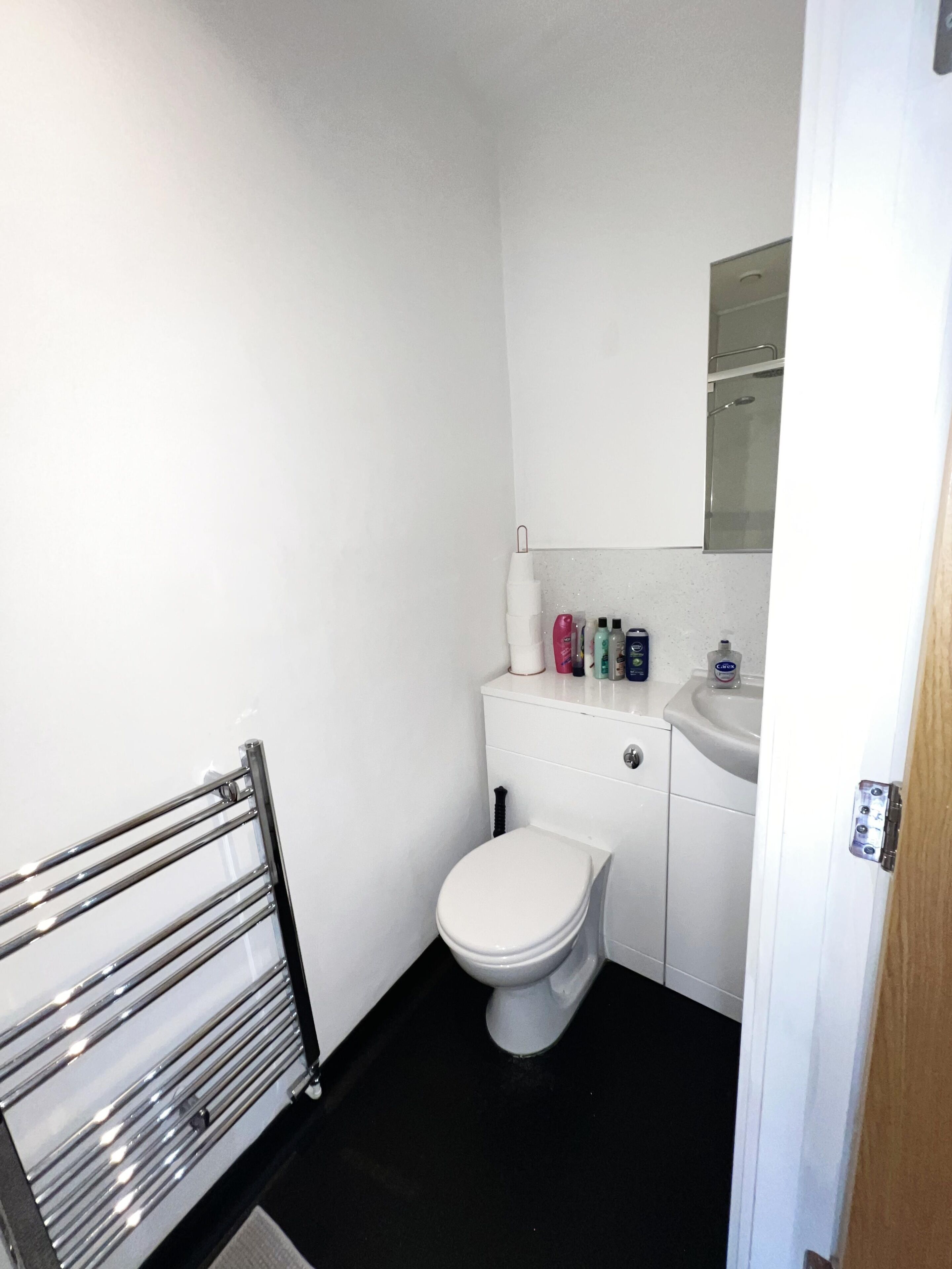 Ein kleines, sauberes Badezimmer mit Toilette, Waschbecken und einem Spiegel darüber. Auf dem Waschbecken liegen Toilettenartikel.