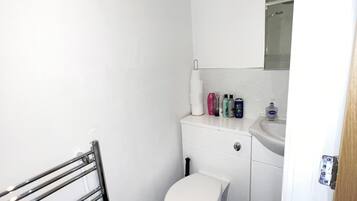 Ein kleines, sauberes Badezimmer mit Toilette, Waschbecken und einem Spiegel darüber. Auf dem Waschbecken liegen Toilettenartikel.