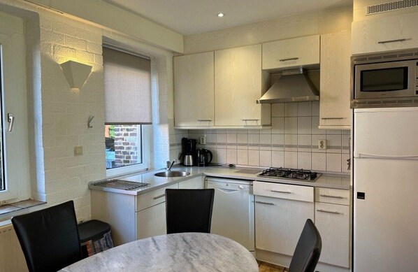 Una cocina compacta con armarios blancos, estufa, microondas y lavavajillas. Hay una ventana con vistas al exterior.