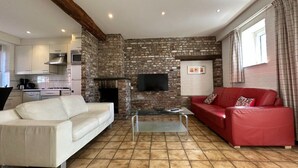 A living room with a stone wall, a fireplace, a TV, a red sofa, and a white sofa. - Bungalowpark Landsrade - Geschakelde Bungalow 9 (Gulpen)