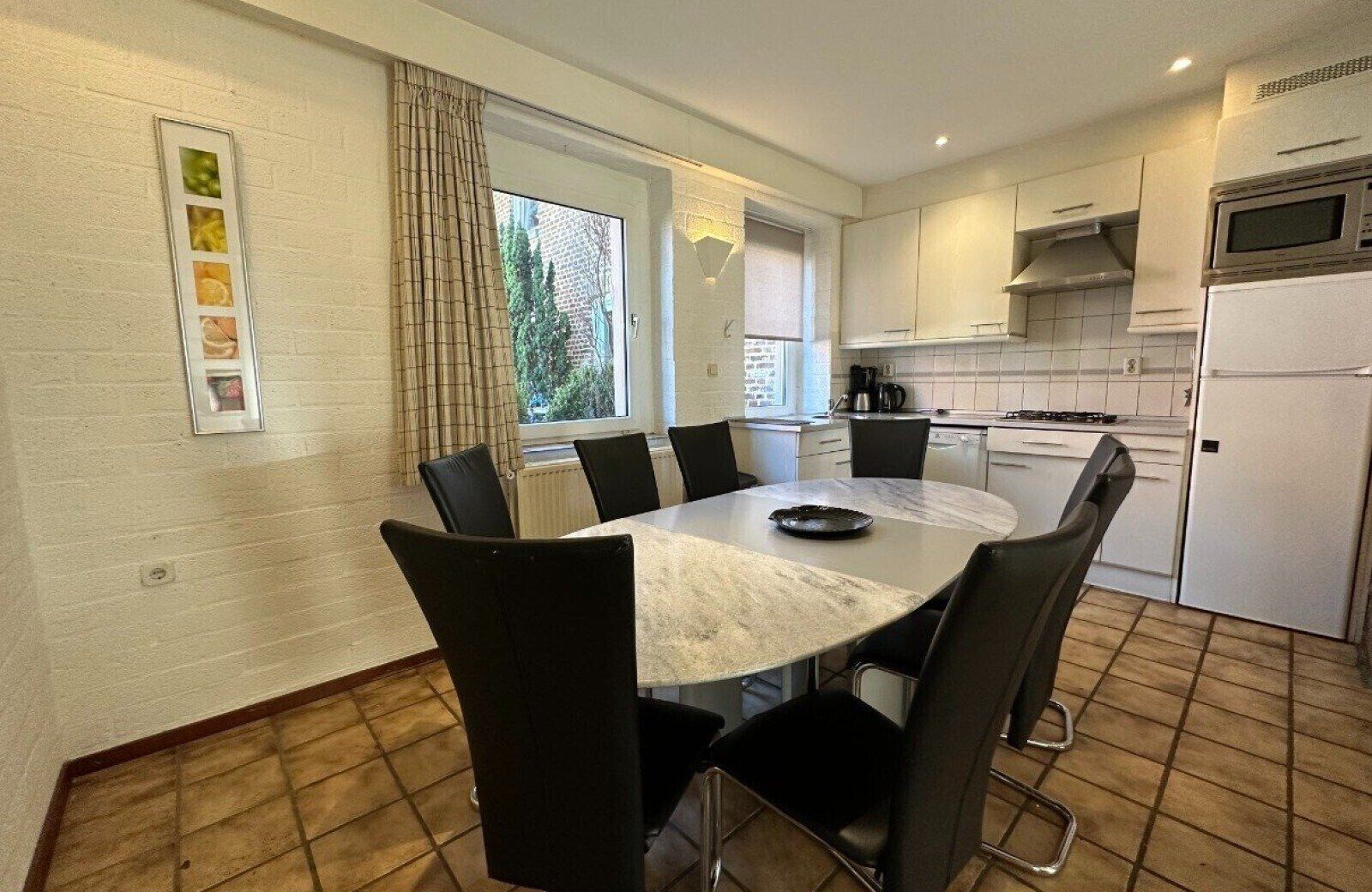 Une cuisine moderne avec des meubles blancs, un four à micro-ondes et une cuisinière. On y trouve une table à manger avec des chaises et une fenêtre avec des rideaux.
