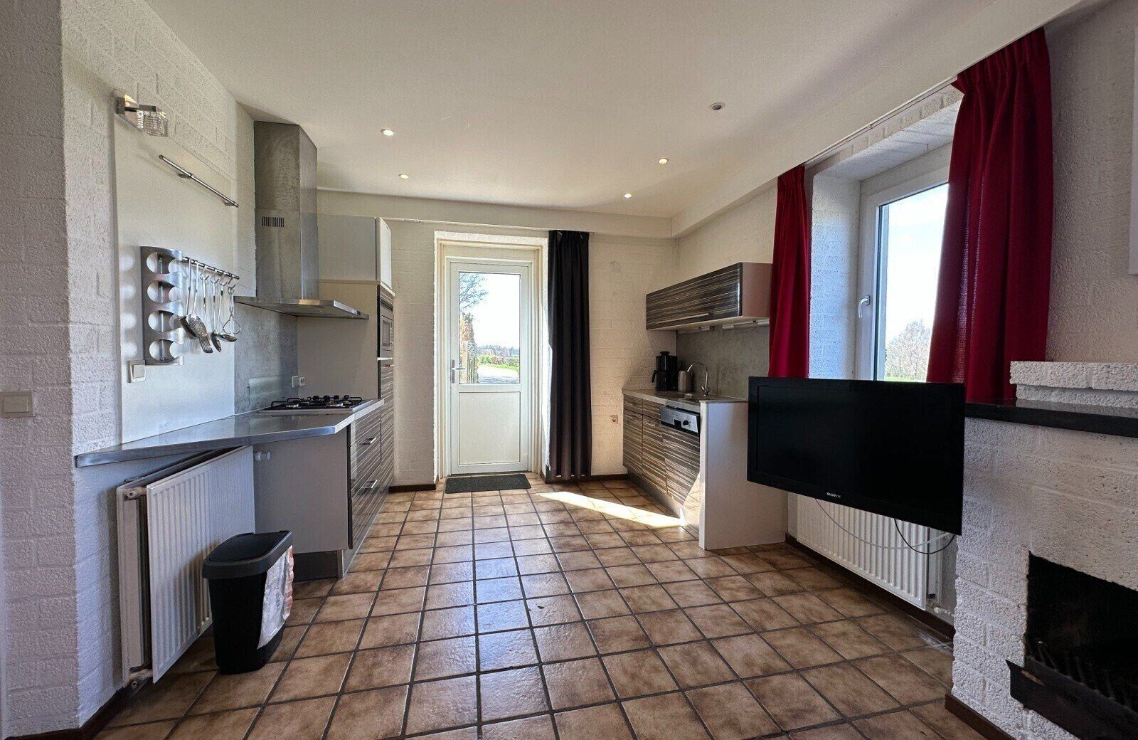 A compact kitchen with a stove, sink, and a flat-screen TV mounted on the wall.