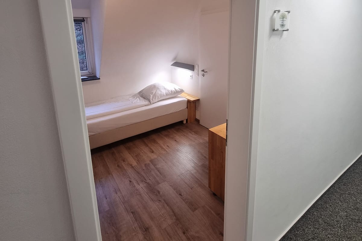 A small, compact bedroom with a single bed, a bedside table, and a nightstand.