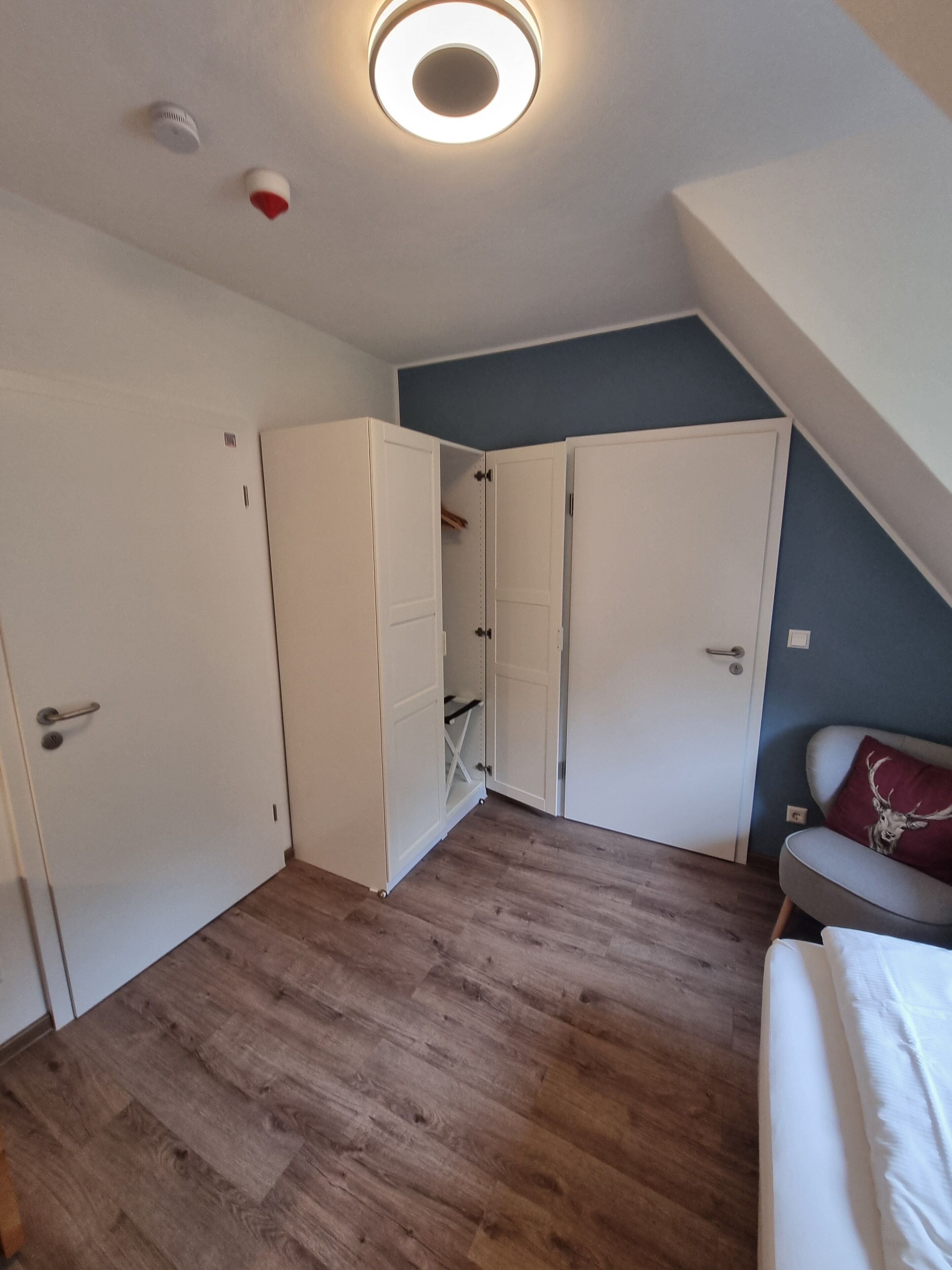 Una habitación compacta con cama alta, armarios blancos, un armario pequeño y suelo de madera.