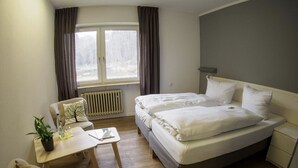 A hotel room with a bed, a desk, a chair, and a window with curtains. - Die Heilsbach (Schönau)
