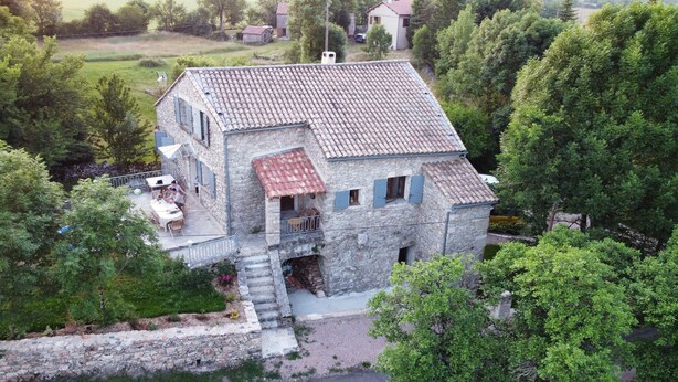 A stone house with a tiled roof, a small balcony, and a staircase leading to the entrance.