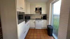 Une cuisine de taille réduite, avec des meubles blancs, un four à micro-ondes, une cuisinière et un lave-vaisselle.