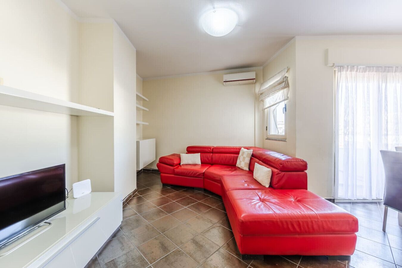 Un soggiorno con un divano in pelle rossa, una televisione a schermo piatto e un mobile bianco.