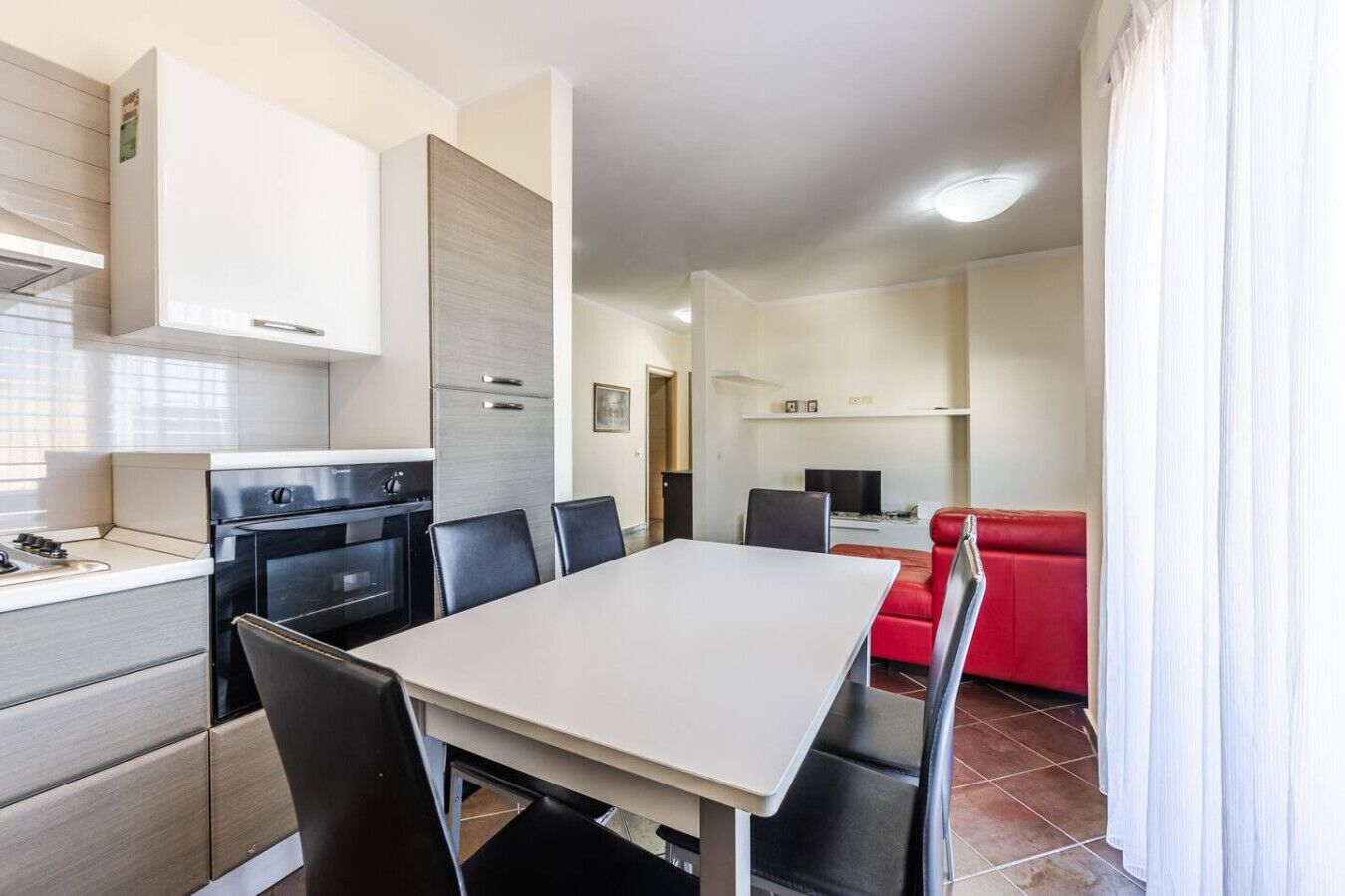 Cocina compacta con comedor, sofá rojo y televisor en la sala.