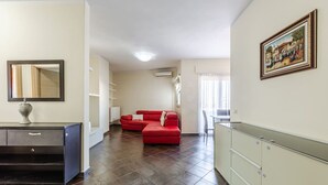 A modern living room with a red sofa, a dining area with a table and chairs, and a kitchen area with cabinets and a countertop. - Spacious Stay in the Heart of Tirana by PikHost (Tiranë)