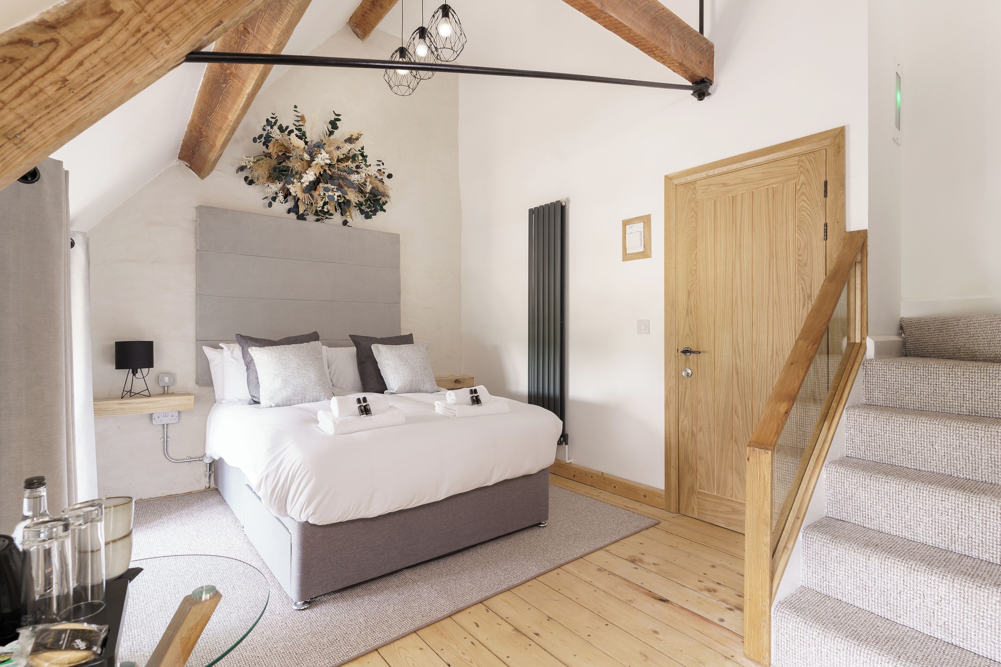 Un dormitorio moderno con una cama grande, una escalera de madera y un techo con vigas a la vista.