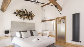 A modern bedroom with a large bed, grey bedding, a wooden ceiling, and a radiator. - The Old House 1147 (Maesteg)