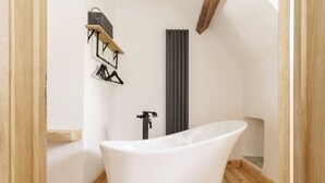 A modern bathroom with a freestanding bathtub, wooden flooring, a towel rack, and a radiator. - The Old House 1147 (Maesteg)