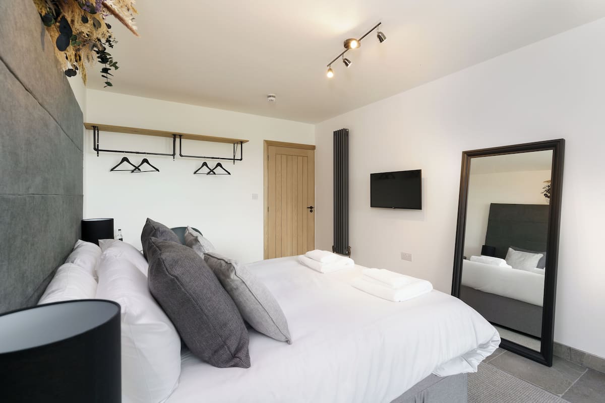 A modern bedroom with a large bed, a bedside lamp, a mirror, and a wall-mounted TV.