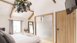 A bedroom with a bed, a wooden door, a shower, and a TV. - The Old House 1147 (Maesteg)
