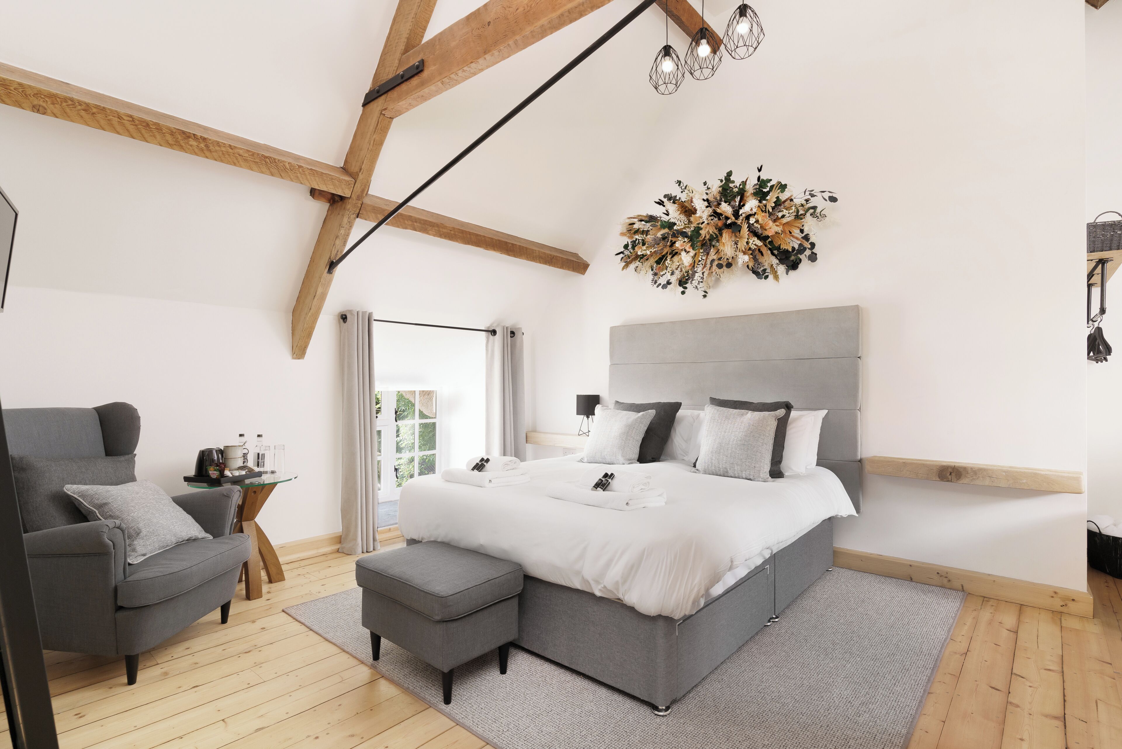 Un dormitorio moderno con una cama grande, un sillón gris, una mesita con una lámpara y un elemento decorativo en la pared.