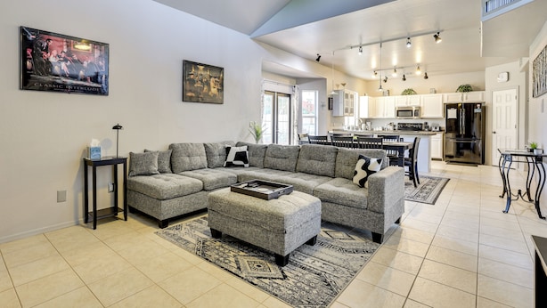 A spacious living room with a sectional sofa, ottoman, and a coffee table. There is a kitchen area with modern appliances and a dining table. - Labor Day Weekend Special: Flexible Check-in/out! (Phoenix)