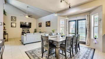 Un vaste espace de vie comprenant une table à manger, des chaises et un canapé. On y trouve également un ventilateur de plafond, un téléviseur à écran plat et une fenêtre avec des rideaux.