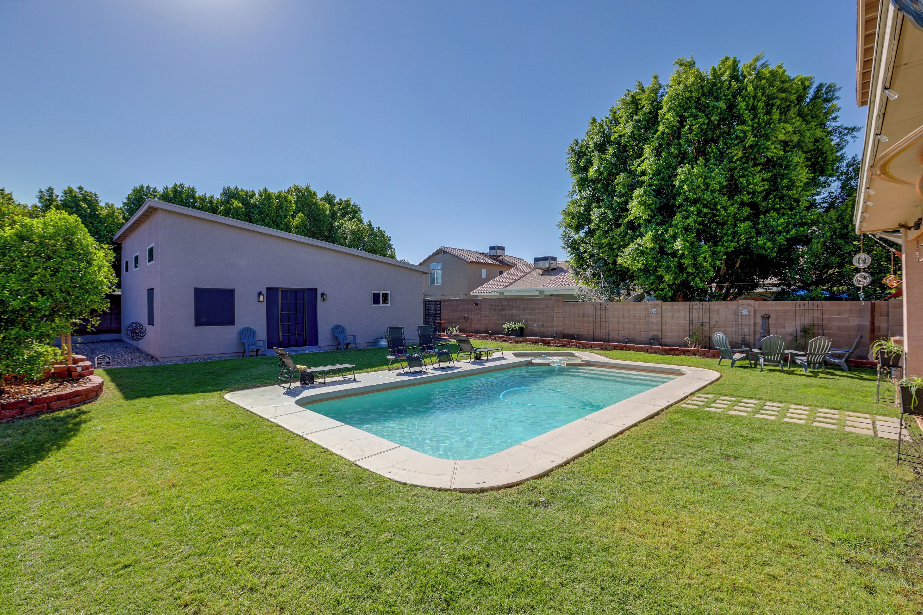 A residential backyard with a swimming pool, a small house, and a large tree.