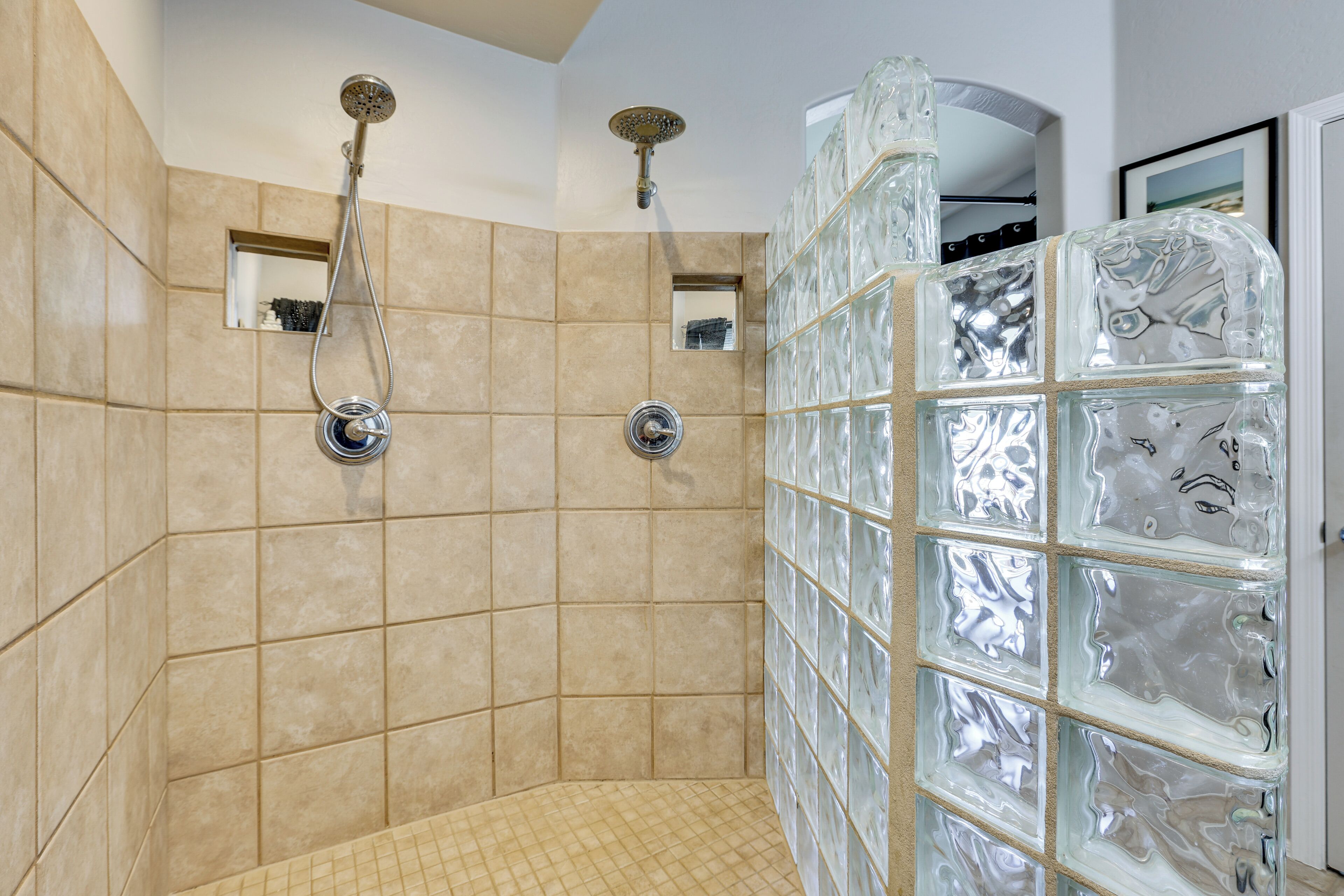 Une douche aux carreaux beiges, un mur en blocs de verre et un petit miroir.