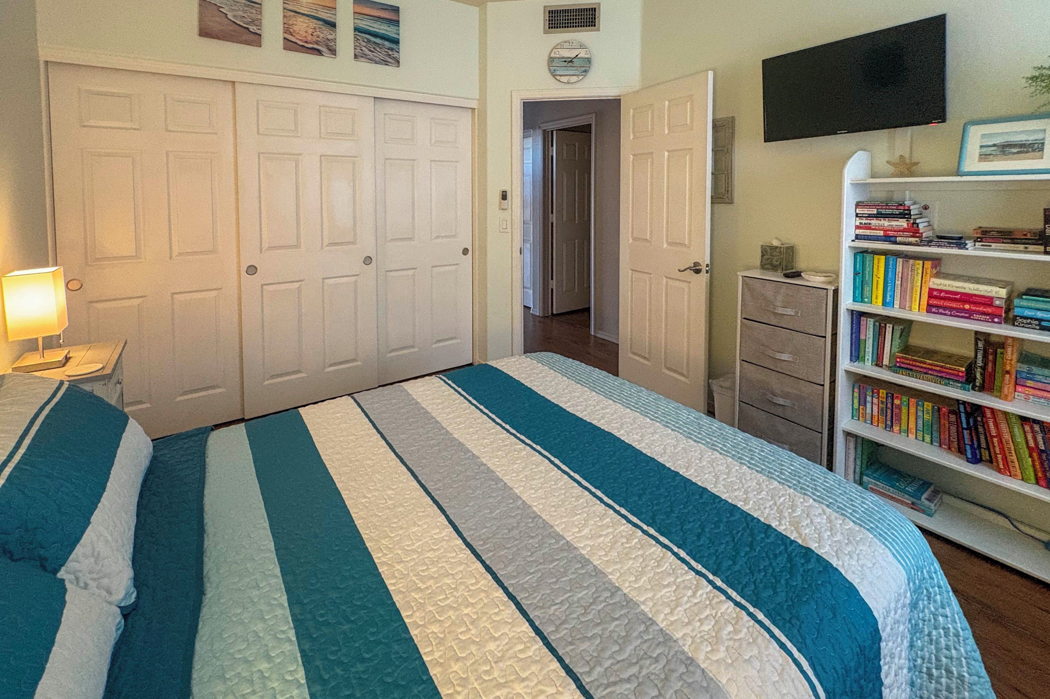 A bedroom with a bed, a bookshelf, a desk, and a door leading to another room.