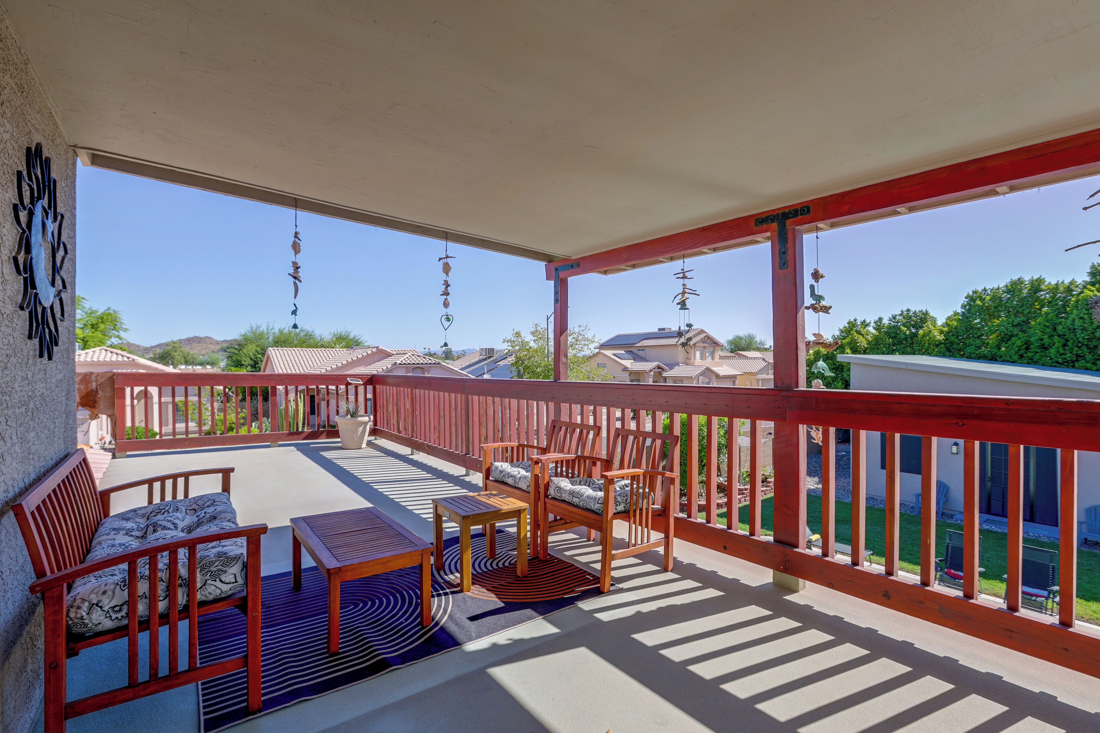 Un balcon abrité, doté de meubles en bois, d’une rambarde rouge et offrant une vue sur les maisons situées au loin.