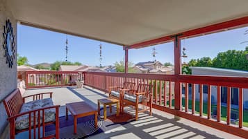 Un balcon abrité, doté de meubles en bois, d’une rambarde rouge et offrant une vue sur les maisons situées au loin.