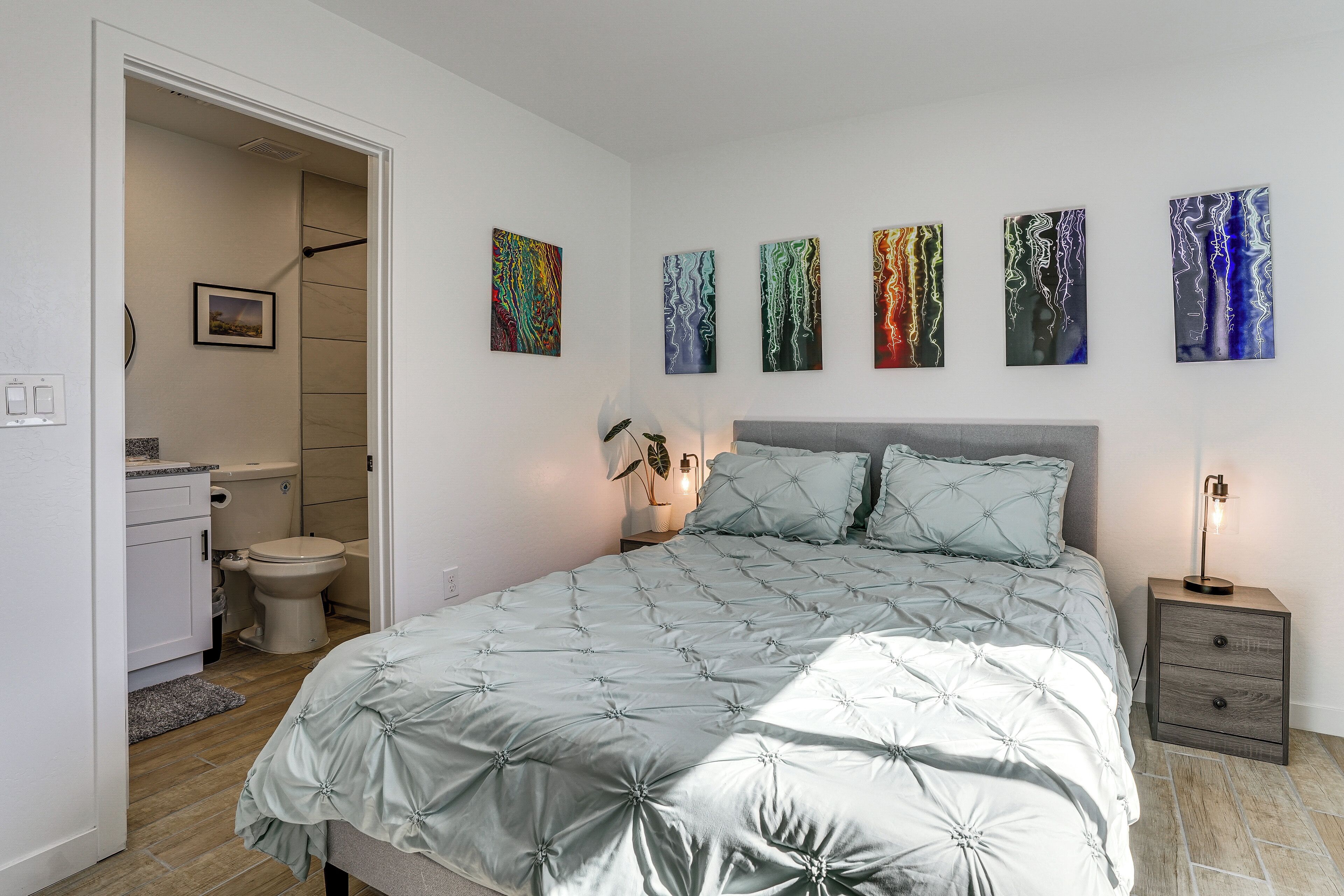 A bedroom with a bed, bedside table, and a nightstand. There are five wall-mounted artworks.