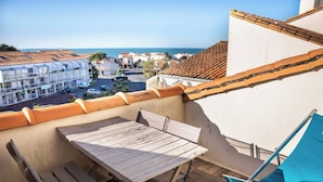 Un balcón con una mesa y sillas de madera, con vistas a un pueblo costero con edificios y un cielo despejado.