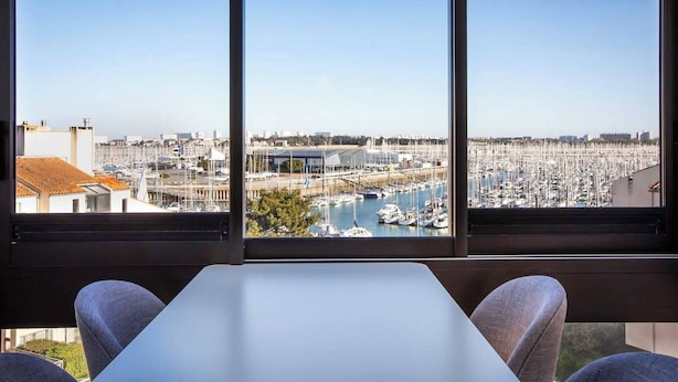 Una habitación con un ventanal grande con vistas a un puerto deportivo con barcos y un paisaje urbano.