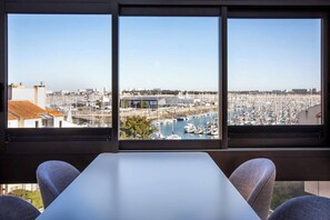 Een kamer met een groot raam dat uitkijkt over een jachthaven met boten en een stadsgezicht.