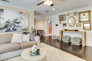 A living room with a beige sofa, a coffee table with books, a large abstract painting, and a ceiling fan.