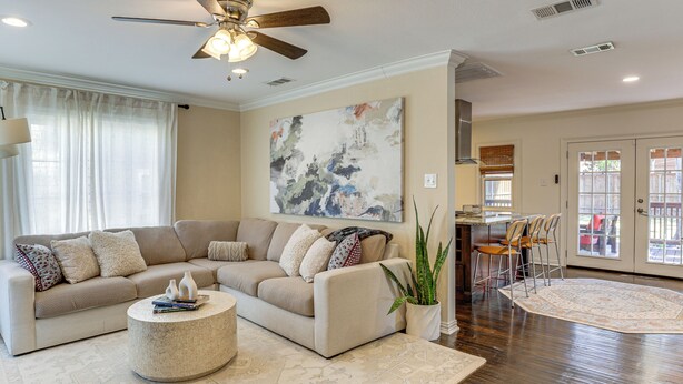 A spacious living room with a beige sectional sofa, a round coffee table, and a large abstract painting on the wall. - 1 Mi to Smu: Home w/ Outdoor Entertainment (Dallas)