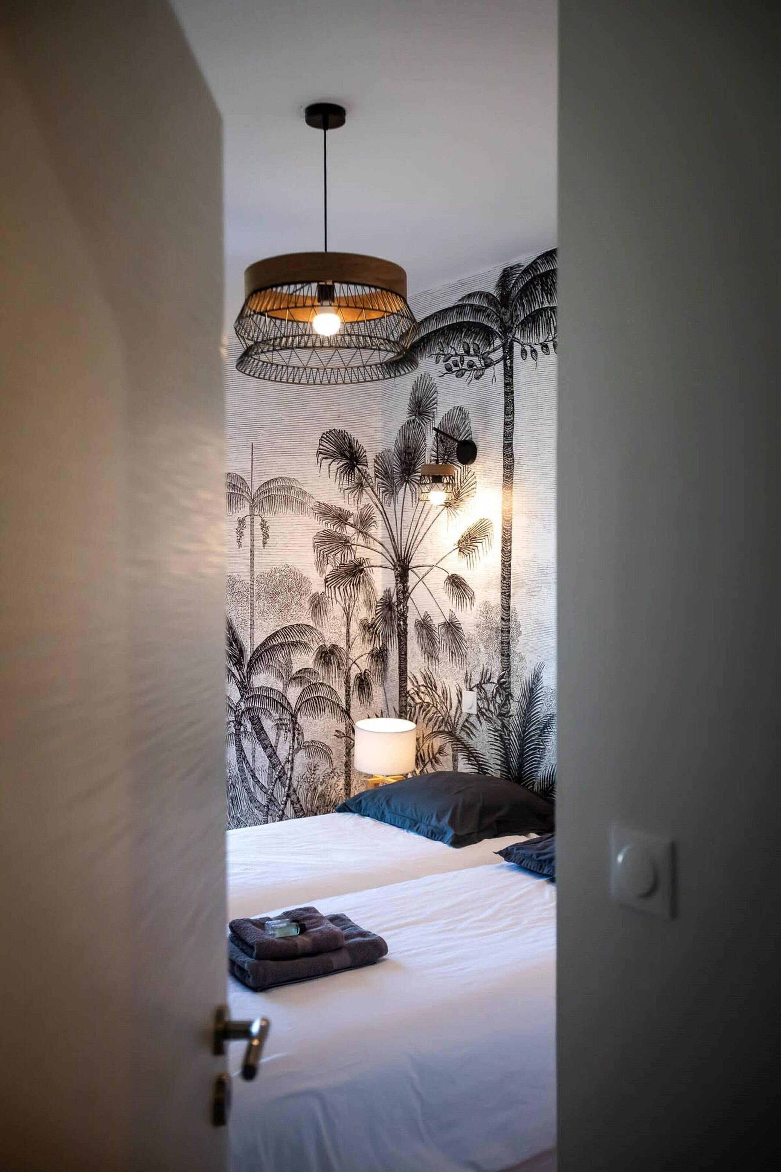 Un dormitorio con cama, lámpara colgante y pared decorada con un mural de plantas tropicales.