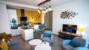 A modern living room with a sofa, two round tables, a TV, and a kitchen area with a dining table and chairs.