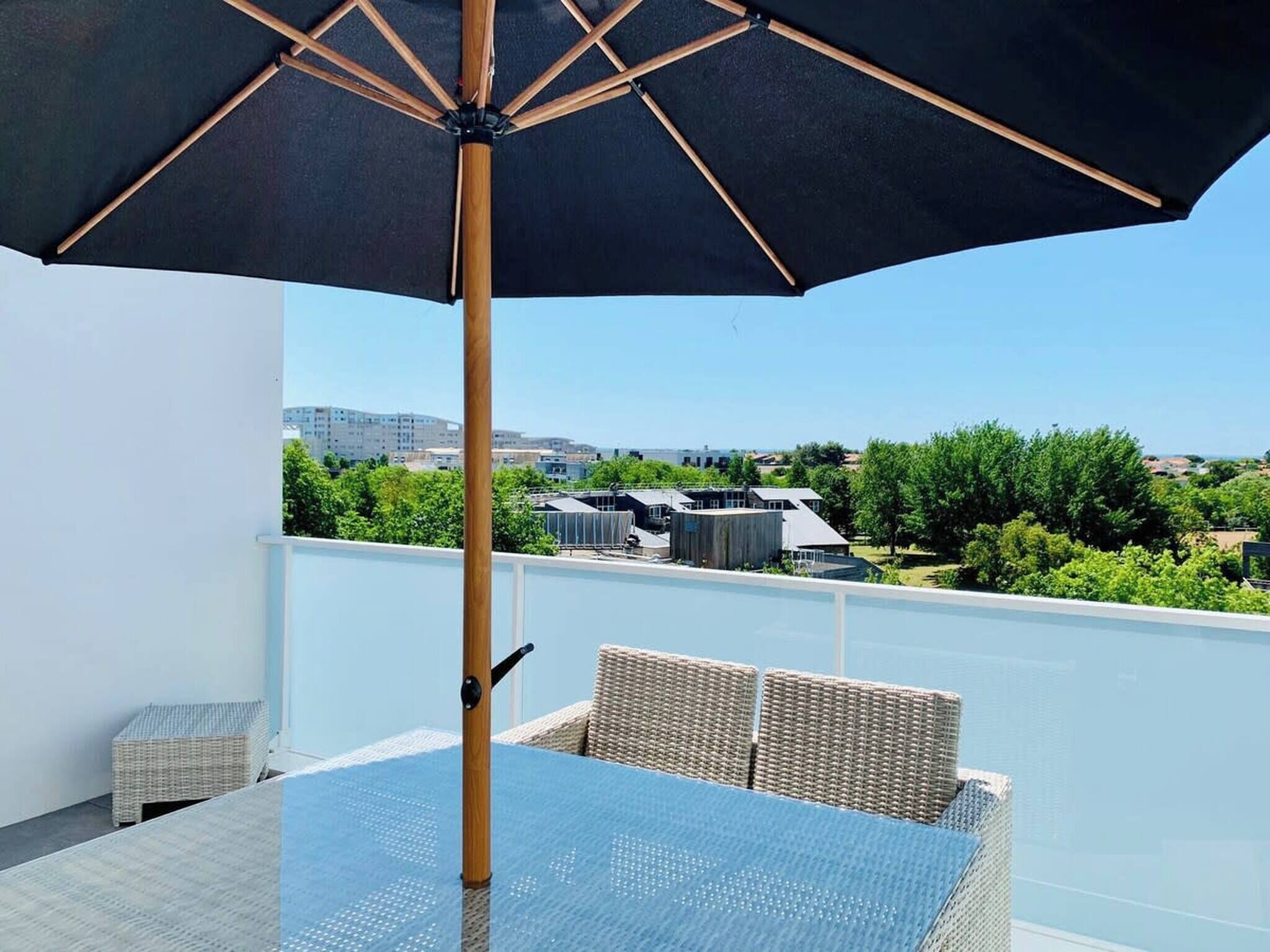 Ein Balkon mit Tisch und Stühlen, einem großen Sonnenschirm und Blick auf Gebäude und Grünflächen.