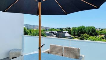 Ein Balkon mit Tisch und Stühlen, einem großen Sonnenschirm und Blick auf Gebäude und Grünflächen.