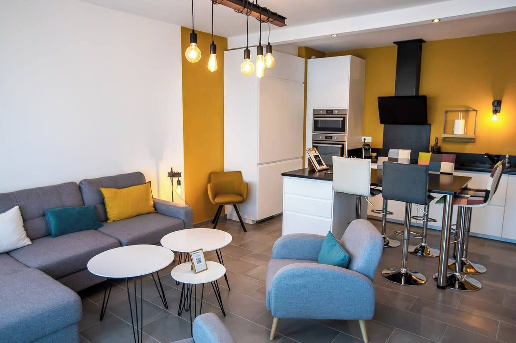 A modern living room with a sofa, two round tables, and a bar area with stools.