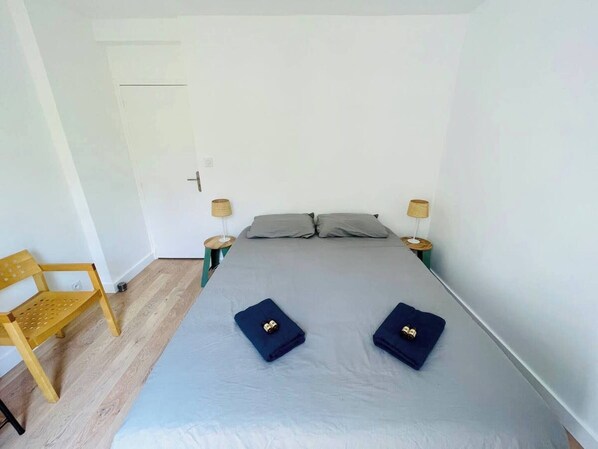 A small, clean room with a bed, two bedside tables, a chair, and a door.