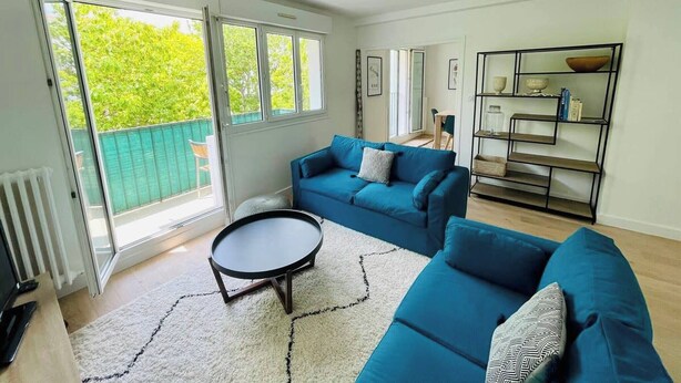 A bright living room with a blue sofa, a small round table, and a bookshelf.