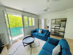 A bright living room with a blue sofa, a small round table, and a bookshelf.